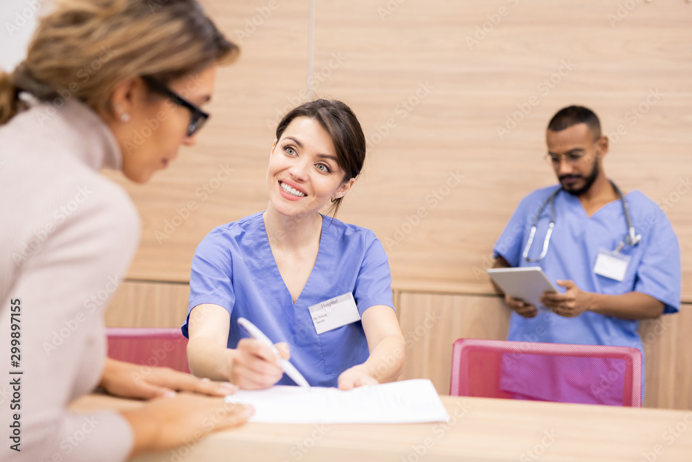 Clinician in uniform smiling at patient while pointing at medical document Clinician in uniform smiling at patient while pointing at medical document