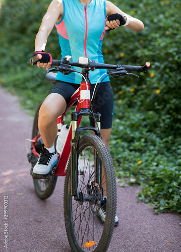 Fototapeta Naklejka Na Ścianę i Meble -  Woman cyclist looking at her smartwatch while riding bike on sunny day