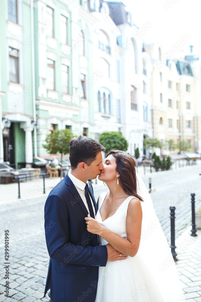Gorgeous wedding couple walking in the city. Groom in a stylish suit and bride in a beautiful white dress, the couple is walking the streets of the city on their wedding day. Together. Wedding concept