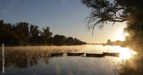 Golden foggy morning on river, movement of mist over water surface, silhouette of old rowing boats. Volume light and flares. Mysterious, calm scene. Rio Negro, Mercedes, Uruguay photo