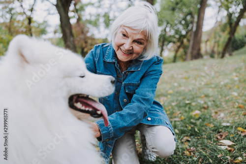 Fototapeta Naklejka Na Ścianę i Meble -  Smiling elderly woman looking at her nice fluffy dog outside