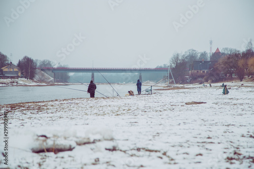 Aspius fishing in early spring when snow is still on the graund. Lot of fisherman with fishing rod stands on the bank of the river.
