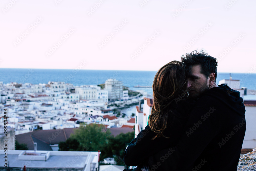 Couple sitting on the roof looking from above to the city in the evening chair. A man with a beard embraces a woman. Happiness to be together.