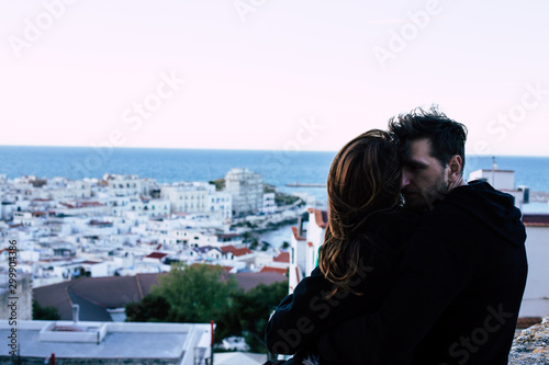 Couple sitting on the roof looking from above to the city in the evening chair. A man with a beard embraces a woman. Happiness to be together.