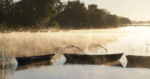 Golden foggy morning on a river, movement of mist over water surface passing through old rowing boats. Volume light and flares. Mysterious, calm scene. Rio Negro, Mercedes, Uruguay photo