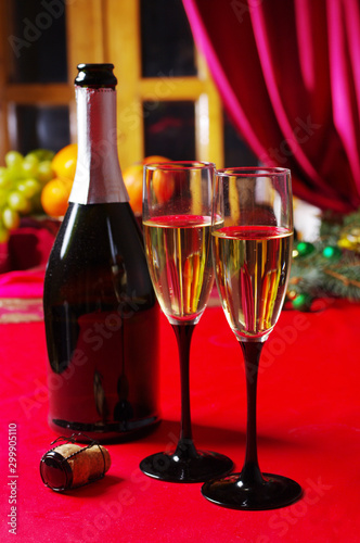 Two glasses of champagne and a bottle on the festive table with a red tablecloth