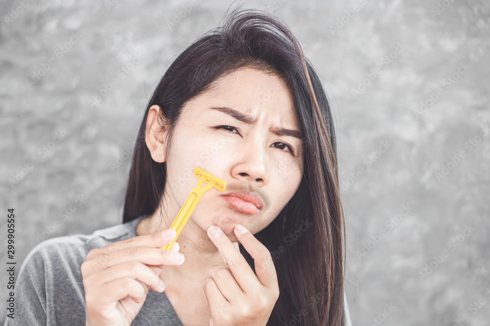 Asian woman shaving mustache on face with a razor Asian woman shaving mustache on face with a razor
