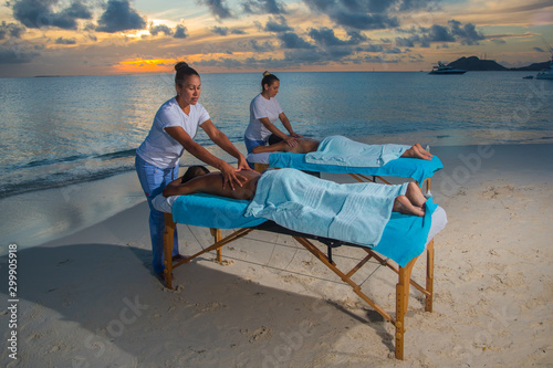 Women giving massage therapy stretch head neck outdoor at Caribbean beach to a couple on the massage table portable to relax. Caribbean turquoise water and sunset beach background .