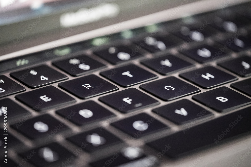 Close-up, shallow focus of a back-lit keyboard seen on a well-known, luxury computer manufacturer. The rear of the image shows part of the defocus screen Close-up, shallow focus of a back-lit keyboard seen on a well-known, luxury computer manufacturer. The rear of the image shows part of the defocus screen