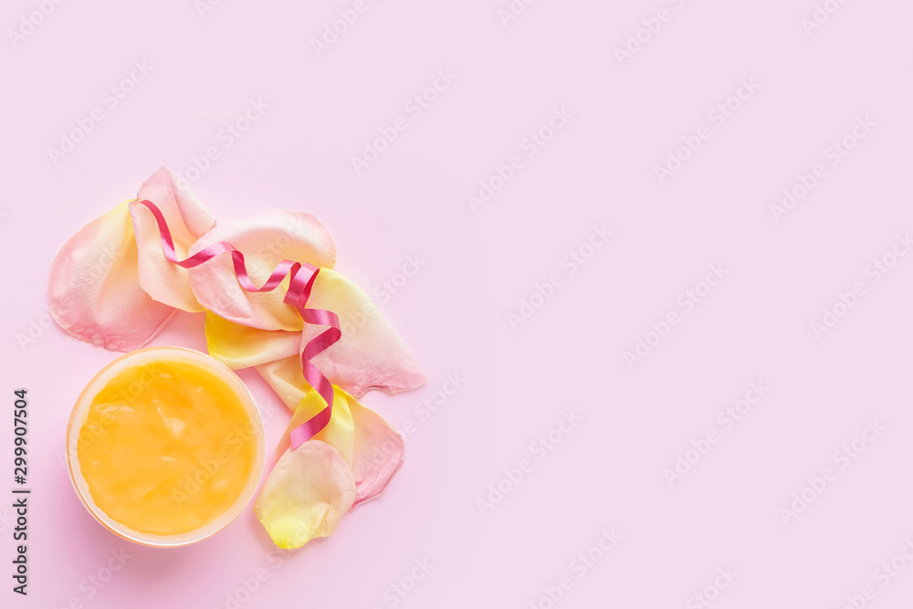 Open jar of cosmetic cream and rose petals on pink background. Concept of organic spa cosmetics. Flat lay, top view, copy space.	