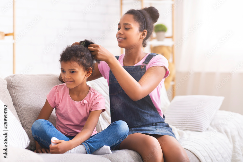 Caring african teenage girl brushing her little sister hair at home Caring african teenage girl brushing her little sister hair at home