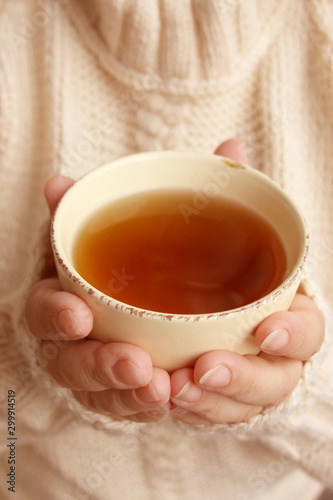 cup of hot fragrant tea in the hands of a woman, texture of a knitted sweater, close-up, copy space, concept of winter or autumn mood