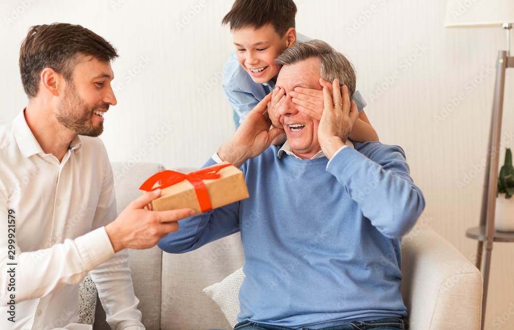 Obraz premium Mature Son And Grandson Congratulating Grandfather Giving Gift Box Indoor