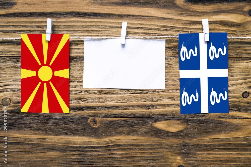 Fototapeta premium Hanging flags of Macedonia and Martinique attached to rope with clothes pins with copy space on white note paper on wooden background.Diplomatic relations between countries.