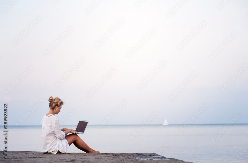 Concentrated female student writing in notebook while learning on the beach , pensive woman freelancer noting information for planning project doing remote job via laptop computer