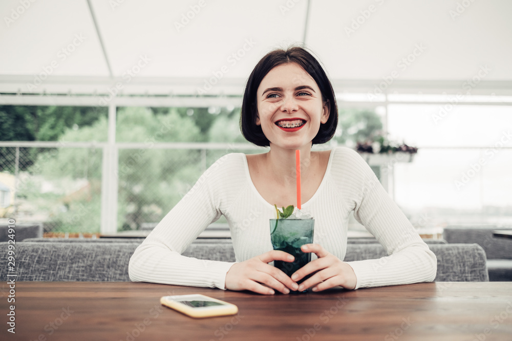 Obraz premium Close Up Portrait of Beautiful Brunette Girl in White Sweater Happy Smile with Dental Braces Drinks Cocktail
