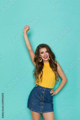 Strong Woman In Jeans Mini Skirt And Yellow Top Is Standing With Fist Raised