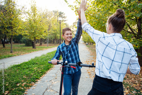 Kids on electric scooters giving each other high-fives.
