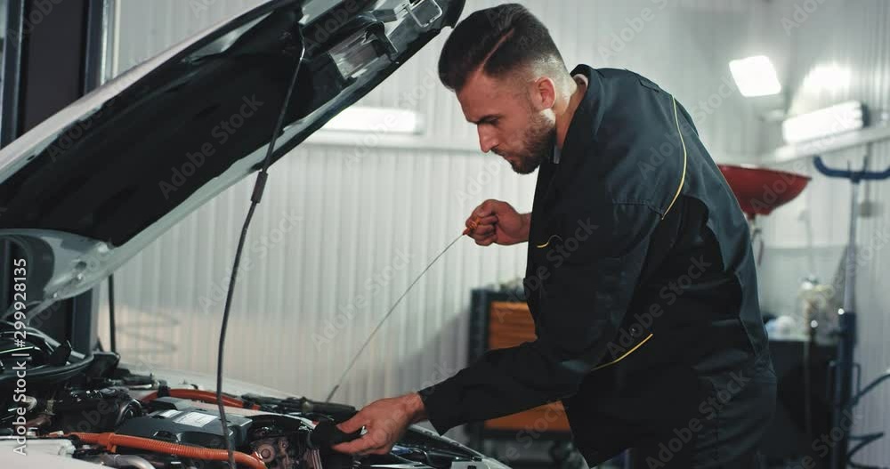 Good looking mechanic guy in a modern service auto checking carefully the oil level from the car Good looking mechanic guy in a modern service auto checking carefully the oil level from the car