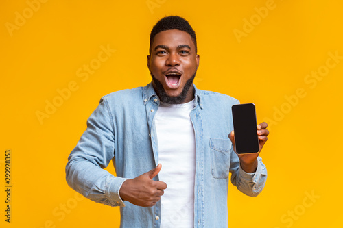 Surprised african man holding smartphone and showing thumb up