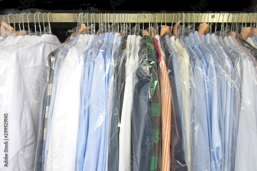 Freshly cleaned men's shirts and ladies blouses in a dry cleaning, hung on hangers and protected by plastic film. Ready for pick up