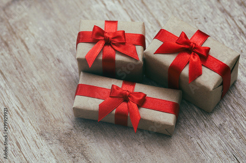 Some gift boxes wrapped in brown craft paper and tie red satin ribbon. Decorative wooden background. Your text space. Set of presents.  © exienator