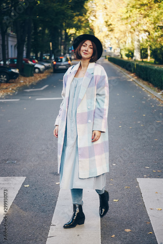 fashion blogger street style. fashionable woman posing wearing oversized checked coat, black ankle boots and a black trendy mini handbag. crossing the street. detail of a perfect fall 2019 outfit. 