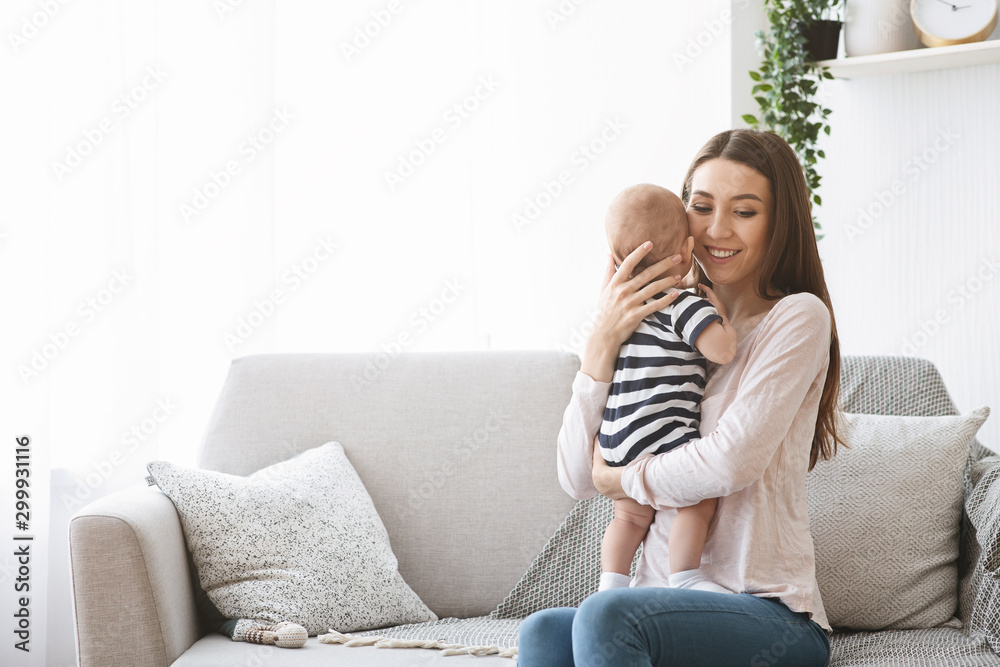 Mother tenderly holding her newborn baby while sitting on sofa