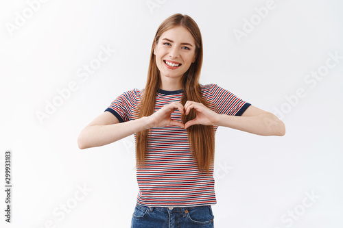 Fotografie Lovely, caring young girlfriend with long fair hair show heart sign, smiling ten