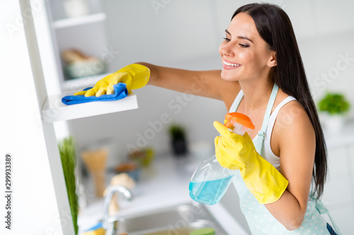 Profile side photo of positive cheerful girl wash shelves in kitchen use spray rubber yellow gloves blue rug feel comfort in modern house
