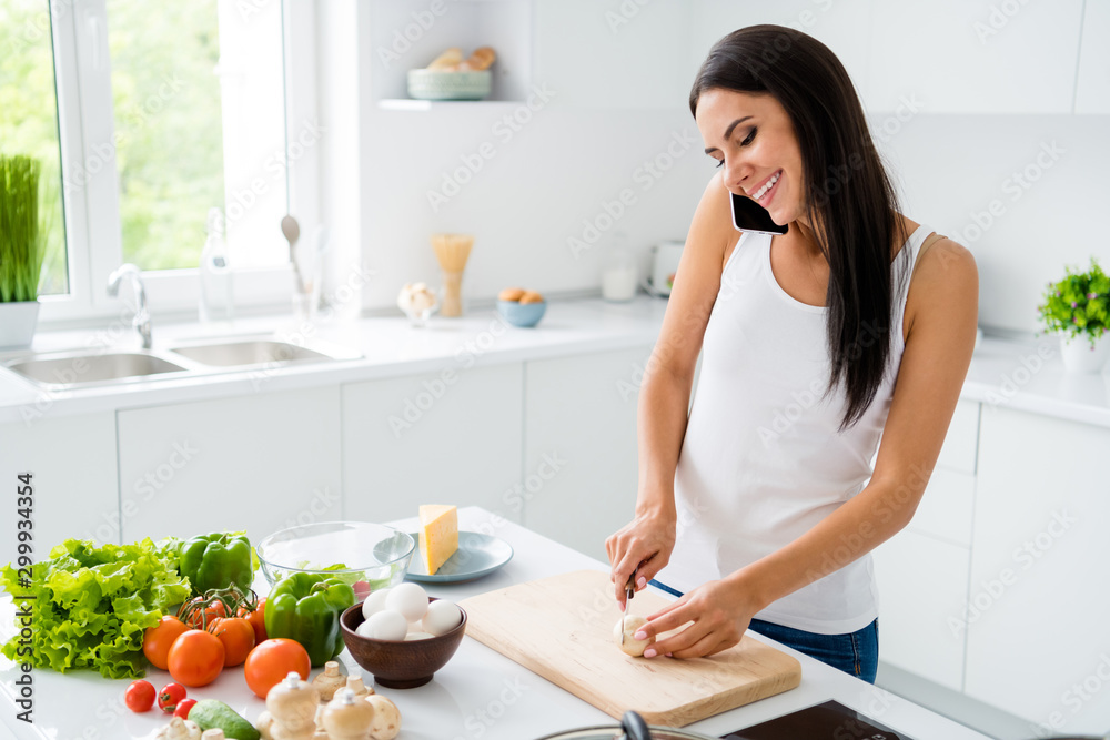 Profile side photo of positive cheerful girl housewife have rest relax want prepare lunch healthcare supper cut champignon on chopping wooden board communicate with friends in house white kitchen