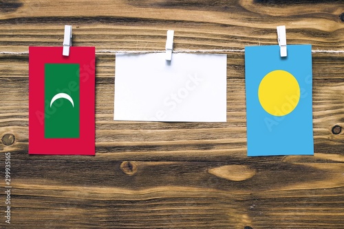 Hanging flags of Maldives and Palau attached to rope with clothes pins with copy space on white note paper on wooden background.Diplomatic relations between countries. photo