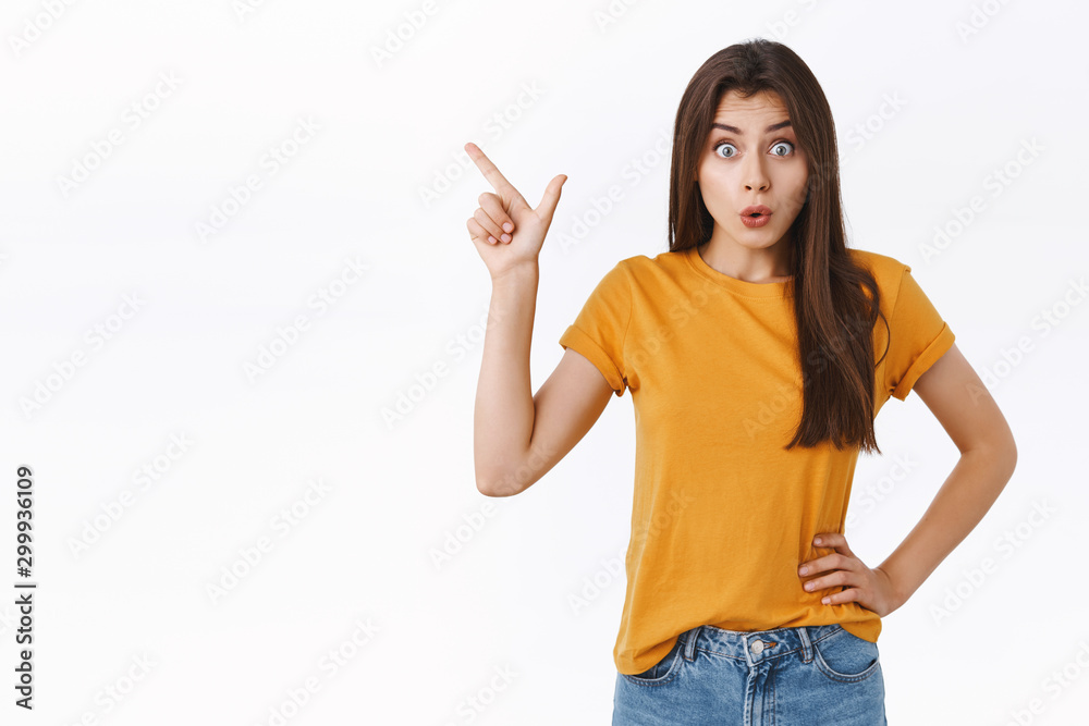 Wondered, impressed good-looking woman in yellow t-shirt, folding lips amazed, say wow and stare camera astonished as discuss new product, pointing upper left corner, checking out cool promo Wondered, impressed good-looking woman in yellow t-shirt, folding lips amazed, say wow and stare camera astonished as discuss new product, pointing upper left corner, checking out cool promo