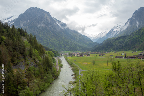 Beautiful panorama view of aare river, meadow and houses in small village in rural area of Switzerland on cloudy sky and mountain background with copy space © Akara