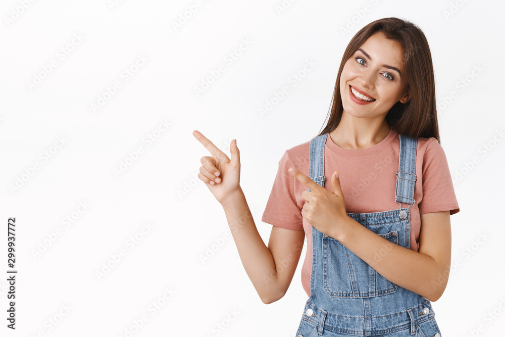 Lovely, alluring cheerful beautiful woman in dungarees, t-shirt, tilt head silly and smiling as promote company product, pointing upper left corner, give advice to check out cool advertisement Lovely, alluring cheerful beautiful woman in dungarees, t-shirt, tilt head silly and smiling as promote company product, pointing upper left corner, give advice to check out cool advertisement