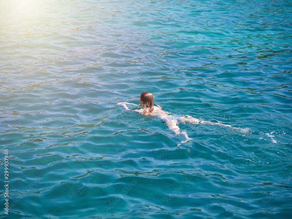 Young slender European girl in swimsuit swimming in clear blue transparent sea water. She enjoying her summer holidays.