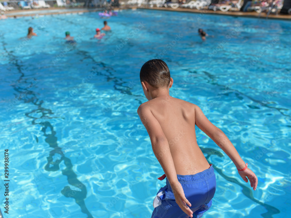 European boy taking off to jump into swimming pool. Back view.