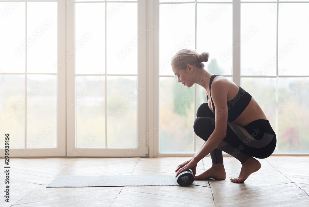 Woman after practicing yoga, rolling yoga mat at studio