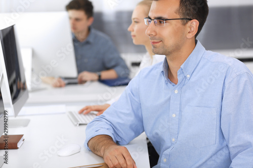 Business people working together in modern office. Focus at happy smiling adult businessman or entrepreneur using pc computer. Teamwork and partnership concept. Casual dress style