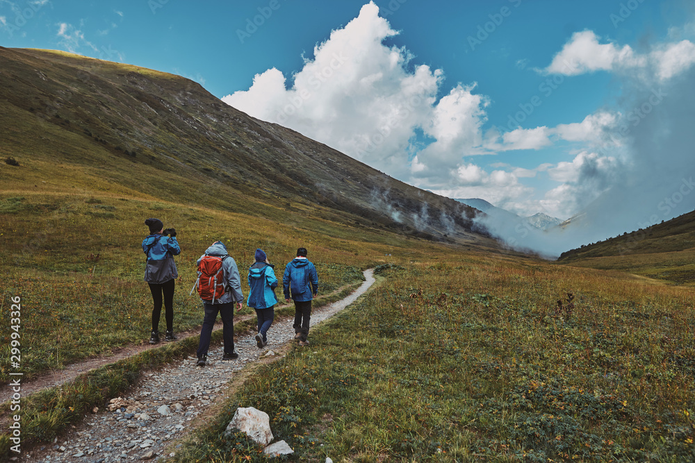 A group of hikers walking down a mountain trail, clouds in a gorge in the background. Bzerpinskiy Karniz