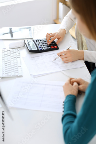 Accountant checking financial statement or counting by calculator income for tax form, hands close-up. Business woman sitting and working with colleague at the desk in office. Audit concept