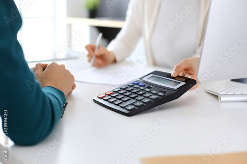 Accountant checking financial statement or counting by calculator income for tax form  hands close-up. Business woman sitting and working with colleague at the desk in office. Audit concept