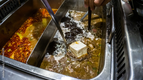The close up view of a metal ladle dipping a cold tofu into a boiling soup