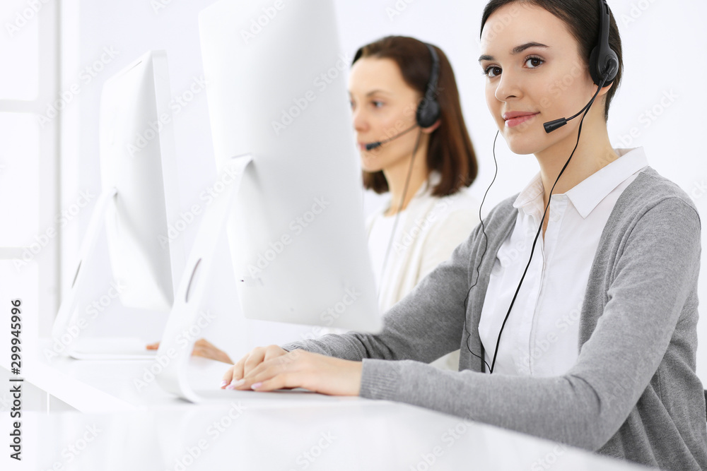 Call center. Beautiful woman receptionist sitting in headset at customer service office. Group of operators at work. Business concept Call center. Beautiful woman receptionist sitting in headset at customer service office. Group of operators at work. Business concept