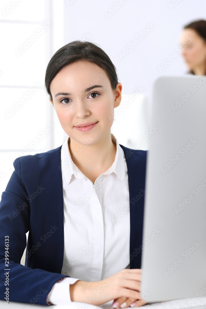 Business woman working with computer in office, female colleague at background. Headshot of Lawyer or accountant at work while sitting at the desk Business woman working with computer in office, female colleague at background. Headshot of Lawyer or accountant at work while sitting at the desk