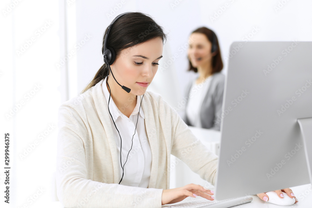 Call center. Beautiful woman receptionist sitting in headset at customer service office. Group of operators at work. Business concept Call center. Beautiful woman receptionist sitting in headset at customer service office. Group of operators at work. Business concept