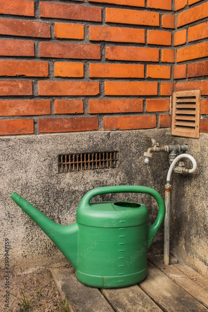 Green watering can standing near old hose. Green watering can standing near old hose.