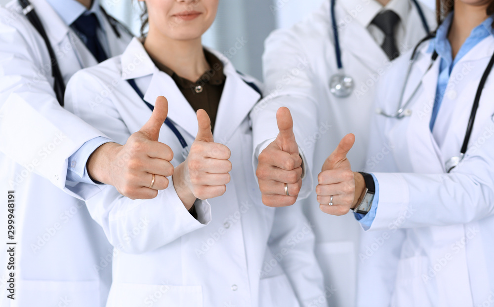 Group of modern doctors standing as a team with thumbs up in hospital office. Physicians ready to examine and help patients. Medical help, insurance in health care, best desease treatment and medicine Group of modern doctors standing as a team with thumbs up in hospital office. Physicians ready to examine and help patients. Medical help, insurance in health care, best desease treatment and medicine