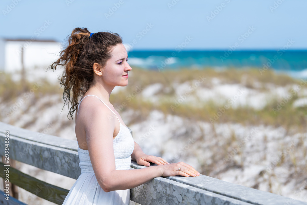 Miramar beach town village in Florida panhandle gulf of mexico ocean water with young happy woman girl in white dress leaning on wooden fence