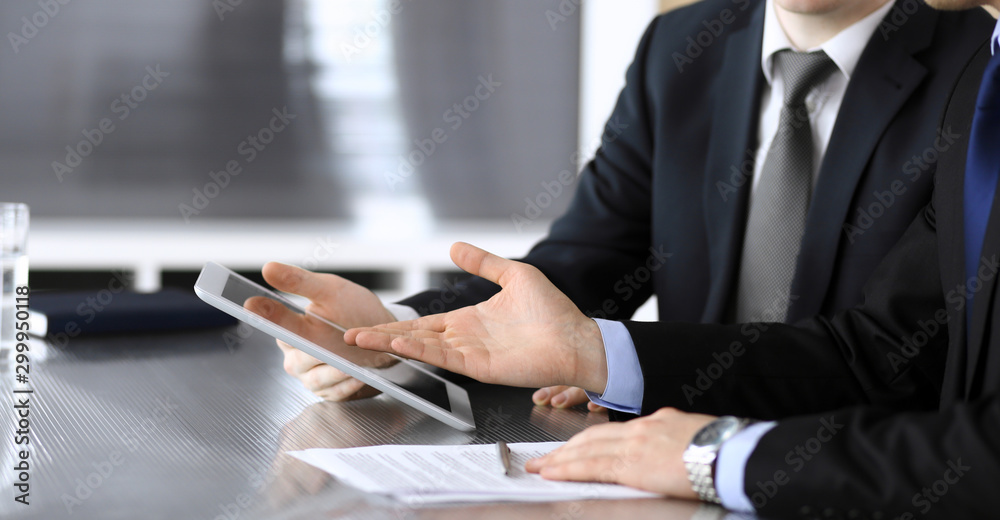 Businessman using tablet computer and work together with his colleague or partner at the glass desk in modern office, close-up. Unknown business people at meeting. Teamwork and partnership concept Businessman using tablet computer and work together with his colleague or partner at the glass desk in modern office, close-up. Unknown business people at meeting. Teamwork and partnership concept